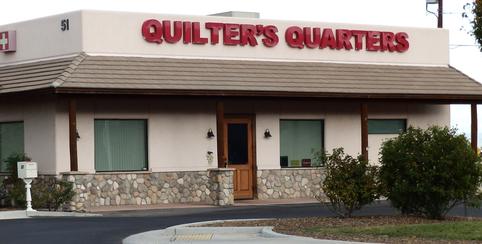 A quilter 's quarters store front with the door ajar.